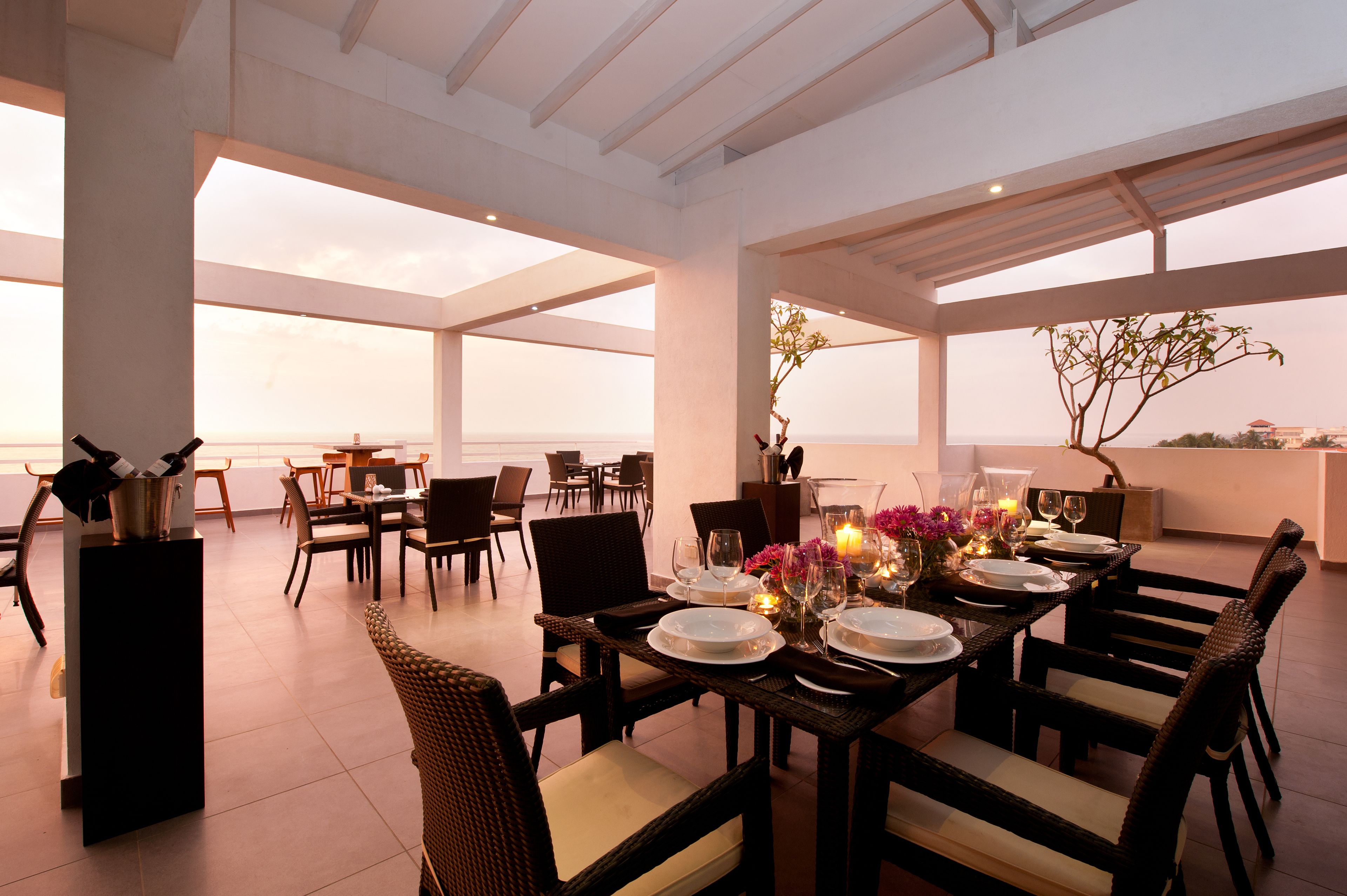 A dining area with a view of the sea, featuring a table set for four with chairs, a buffet area, and a large window overlooking the ocean.