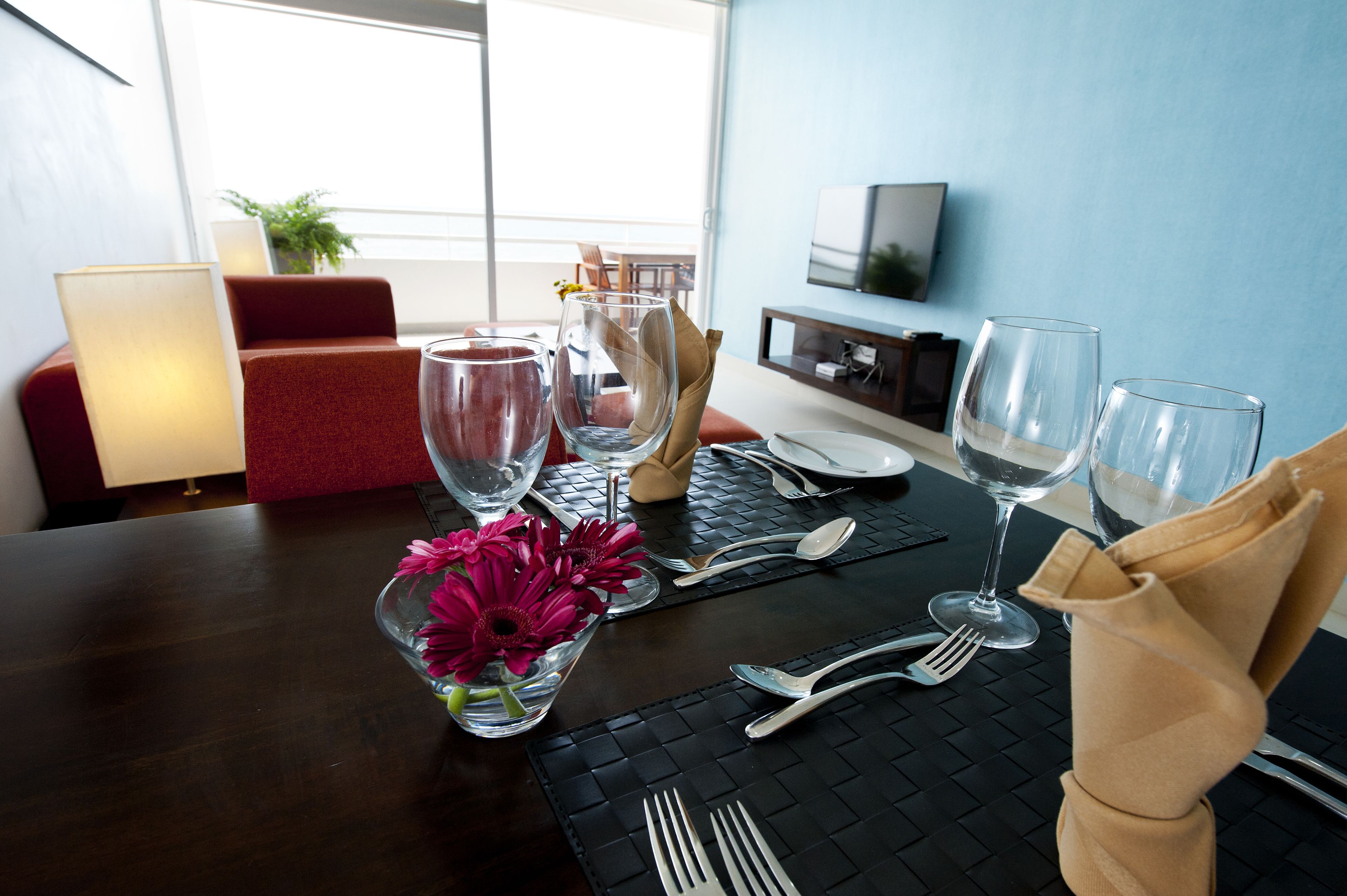 A dining table set with clear glasses, cutlery, and a vase with flowers.