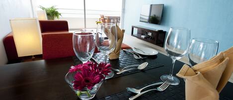A dining table set with clear glasses, cutlery, and a vase with flowers.