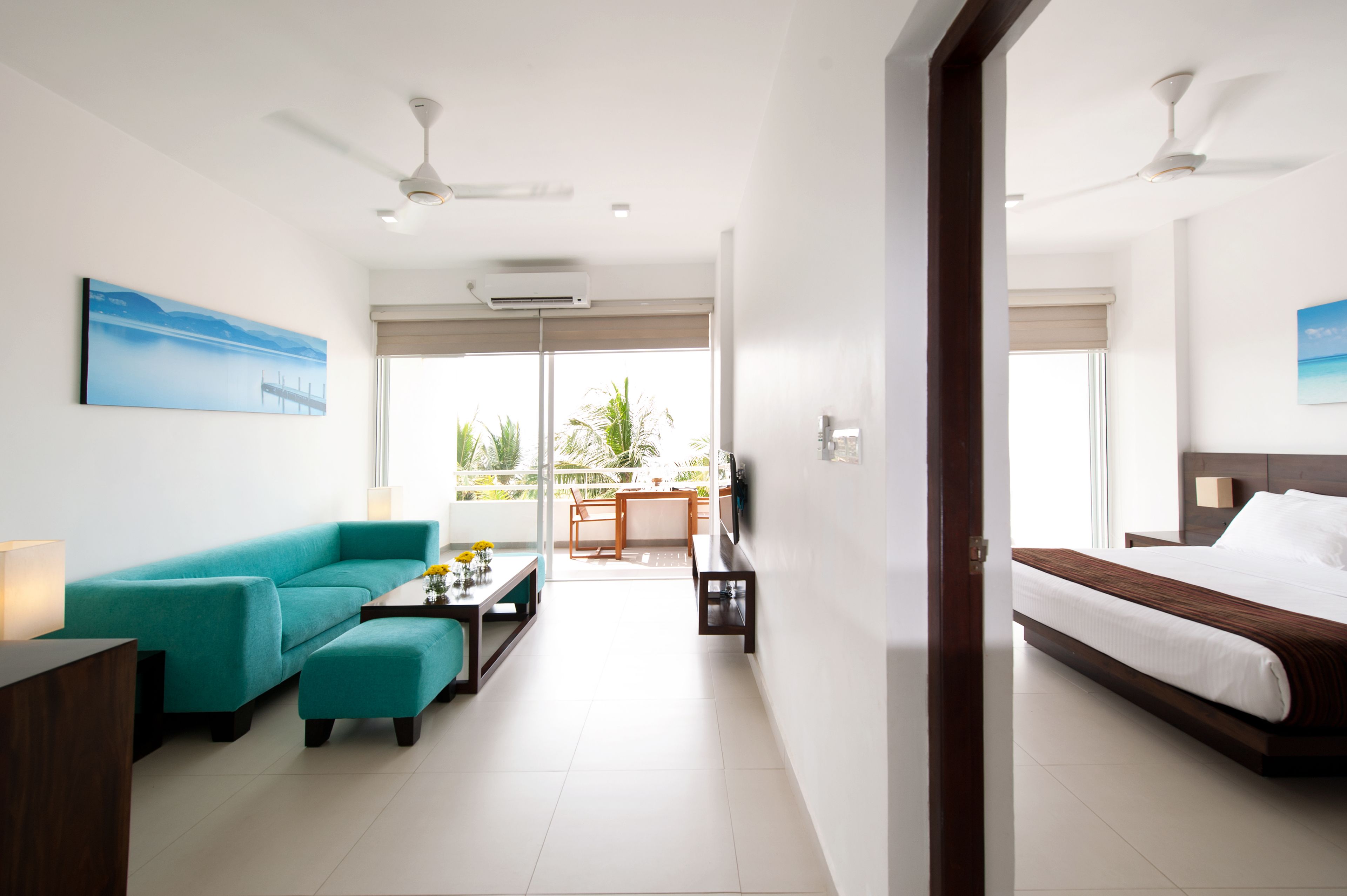 A modern hotel room with a bed, a sofa, a coffee table, and a balcony with a view of greenery.