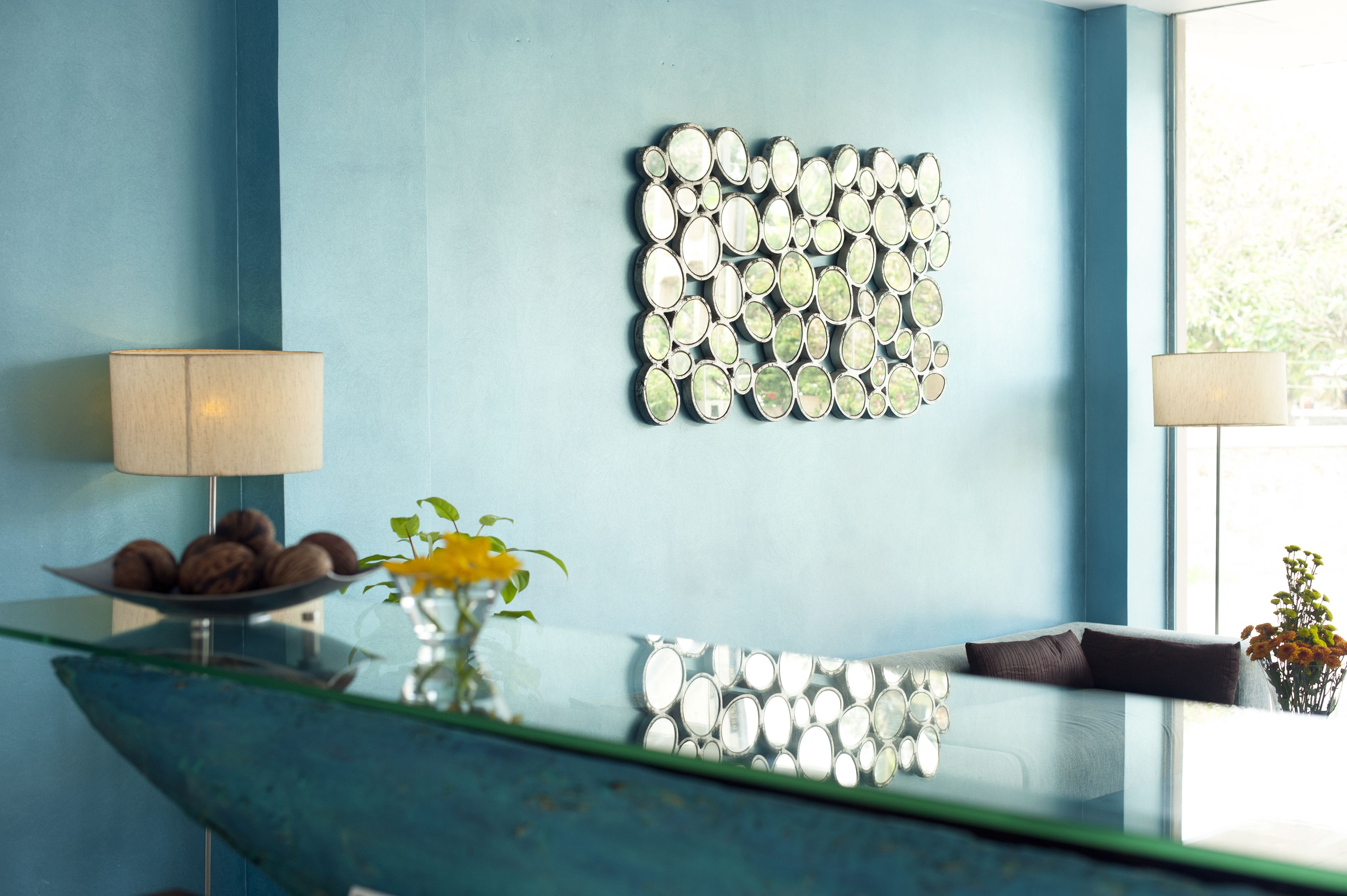 A reception area with a blue wall, a decorative mirror, a glass table with a bowl of cookies, and a vase with flowers.