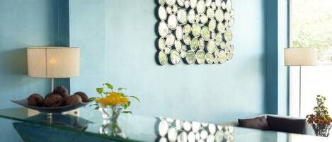 A reception area with a blue wall, a decorative mirror, a glass table with a bowl of cookies, and a vase with flowers.