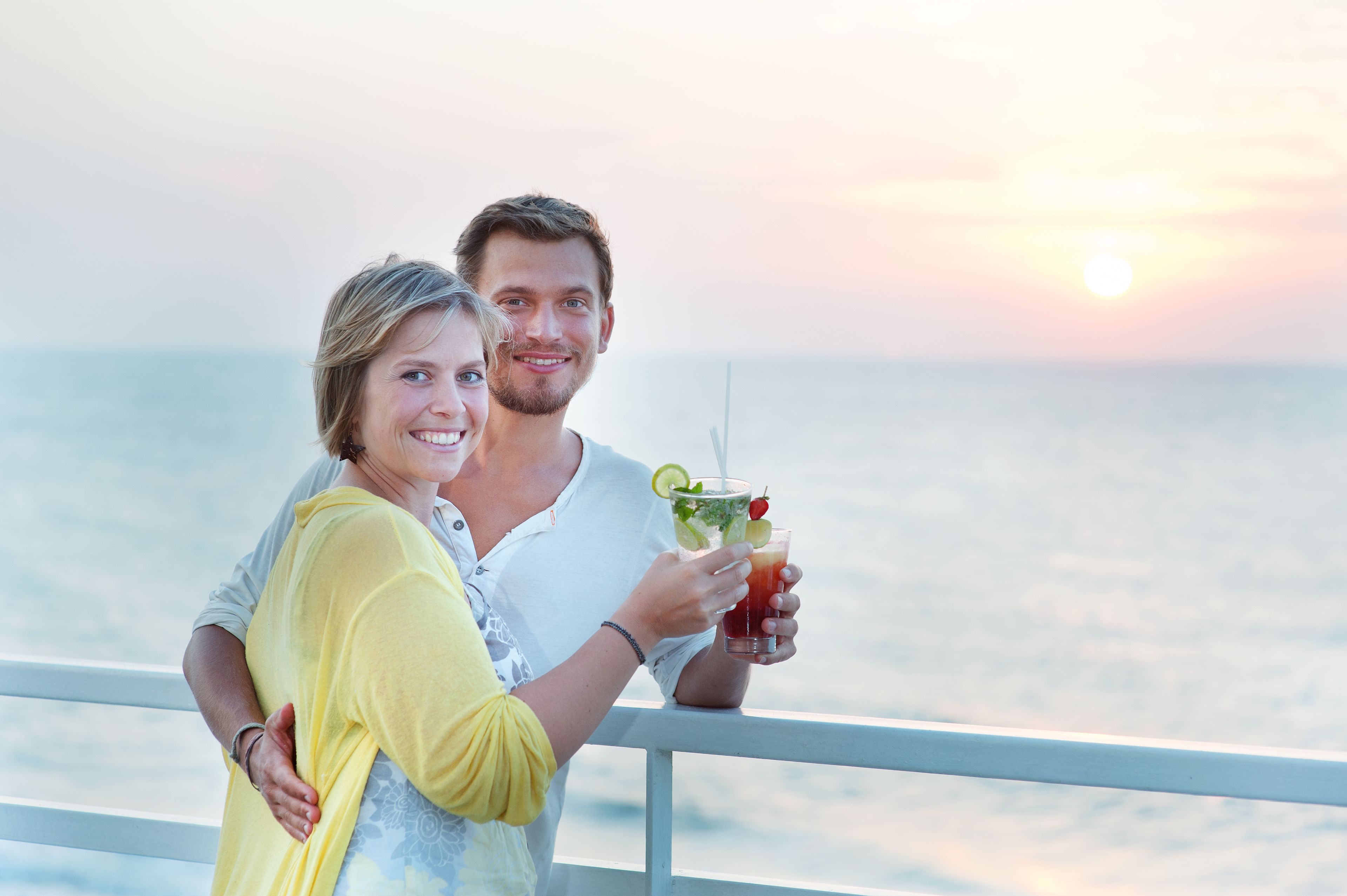 A couple standing by a railing with a sunset in the background.