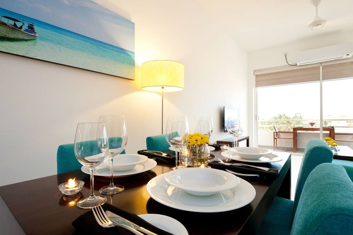 A dining table set with plates, glasses, and cutlery, a vase with yellow flowers, and a lit candle.