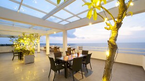An outdoor dining area with a glass ceiling, tables, chairs, and a view of the sea. - The Beach Apartments (Negombo)