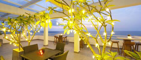 An indoor patio with tables and chairs, surrounded by potted plants and string lights.