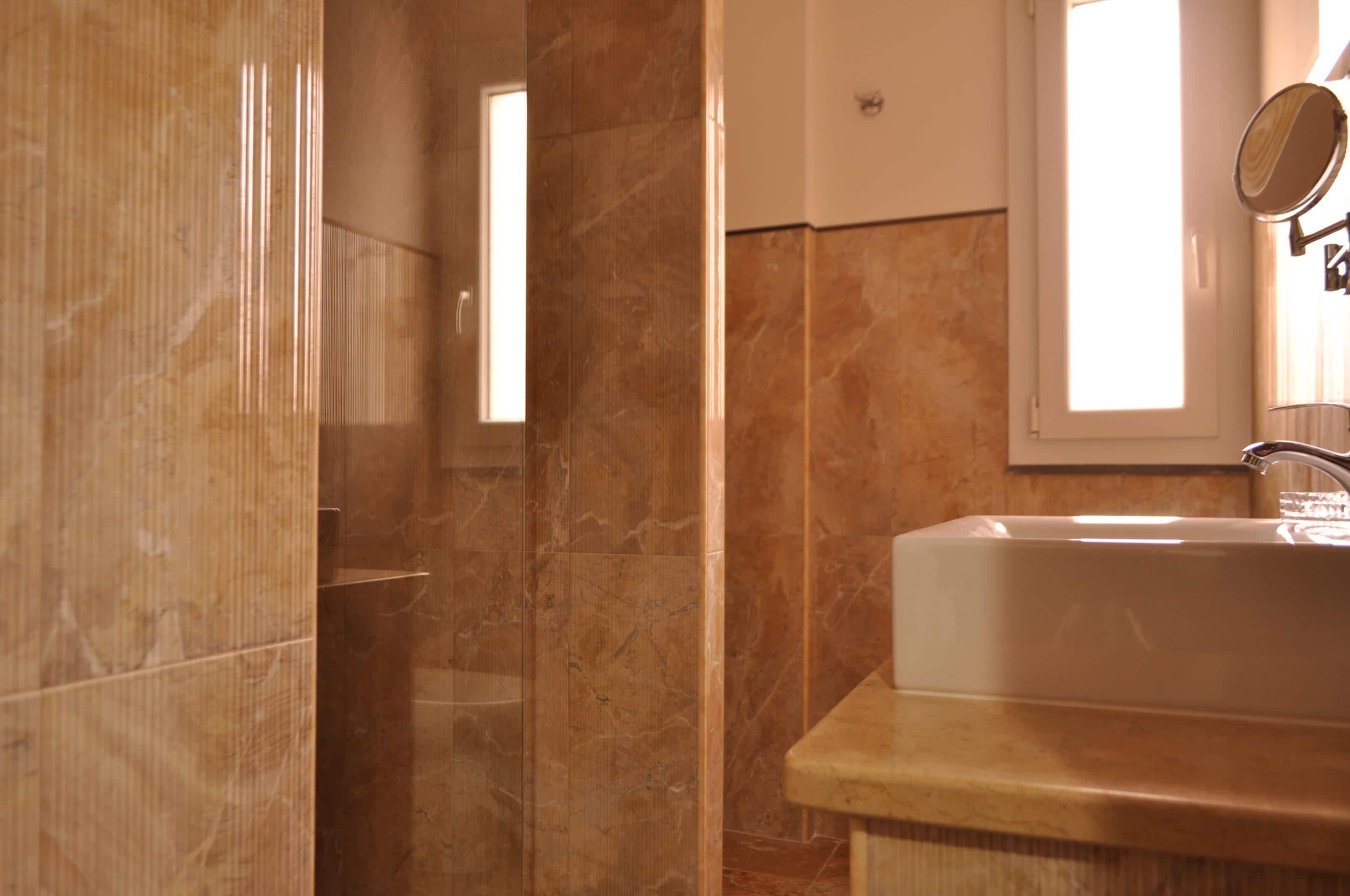 Bagno con parete in marmo, lavandino e specchio.