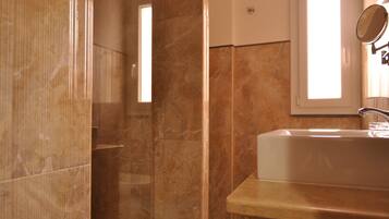Bagno con parete in marmo, lavandino e specchio.