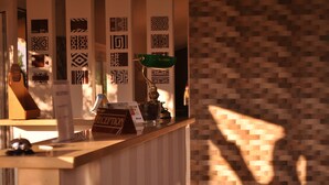 Un comptoir d’accueil agrémenté de motifs décoratifs sur les murs, une lampe de bureau verte et un panneau indiquant la réception.
