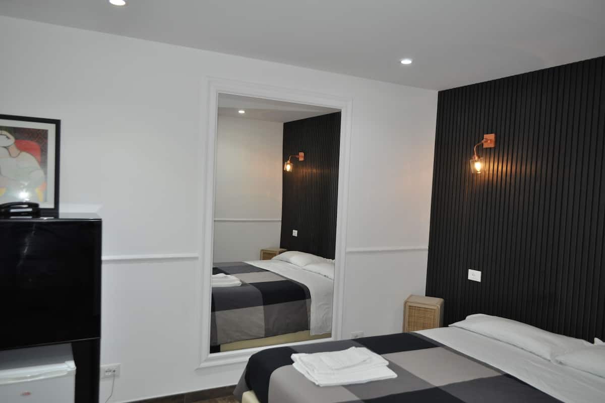 Une chambre d’hôtel avec un lit, une télévision, une petite table et un miroir.