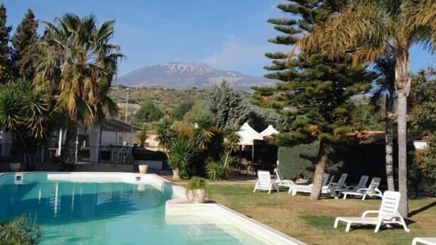 Une piscine entourée de chaises longues, de palmiers, avec une montagne en toile de fond.