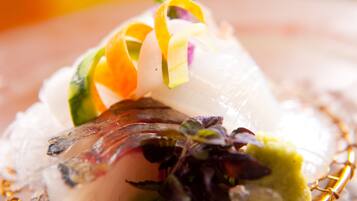 A close-up of a dish with thinly sliced fish, garnished with colorful strips and greens.
