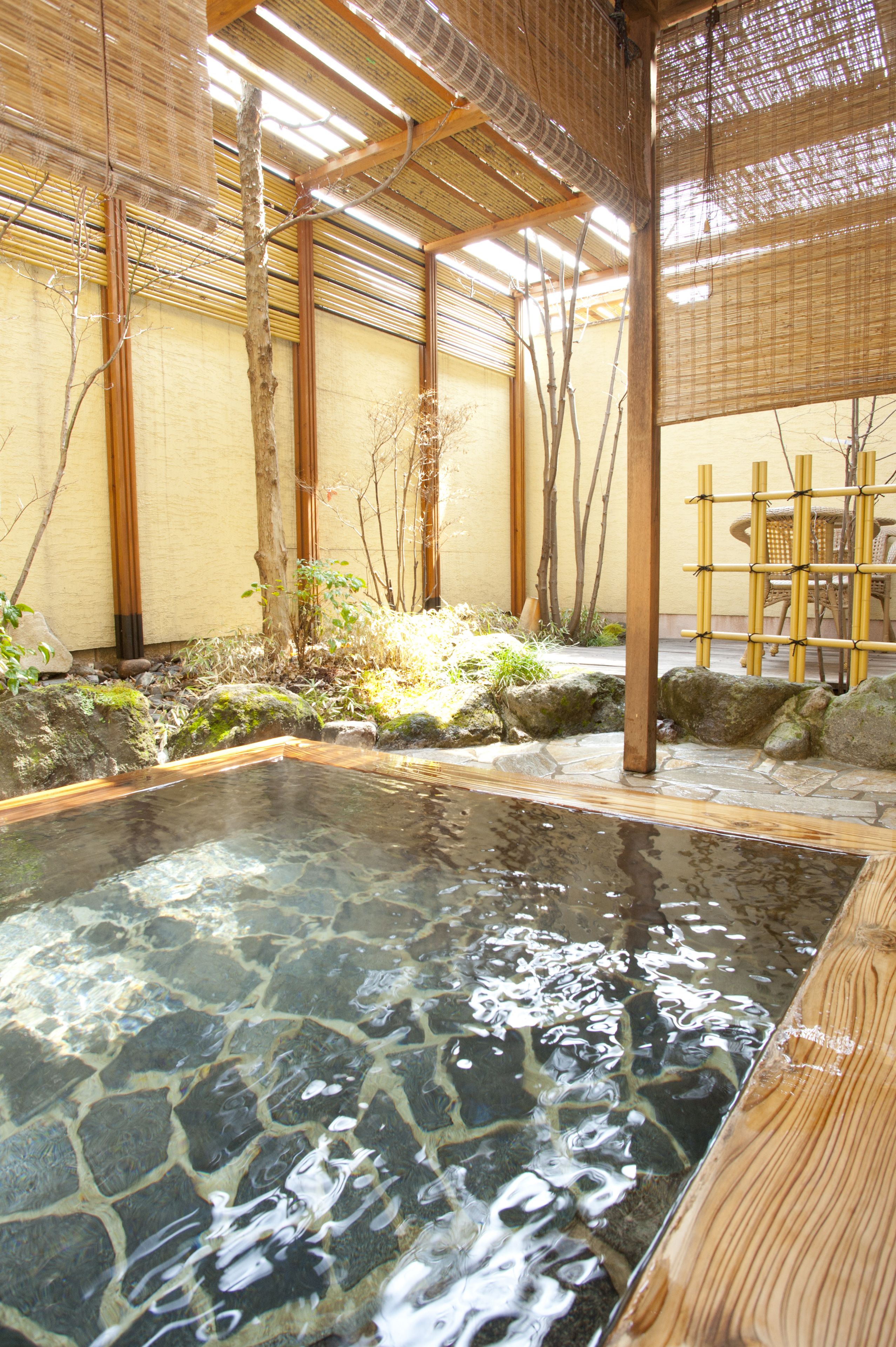 Uma onsen japonesa tradicional com banheira de pedra, estruturas de bambu e uma mesa de madeira.