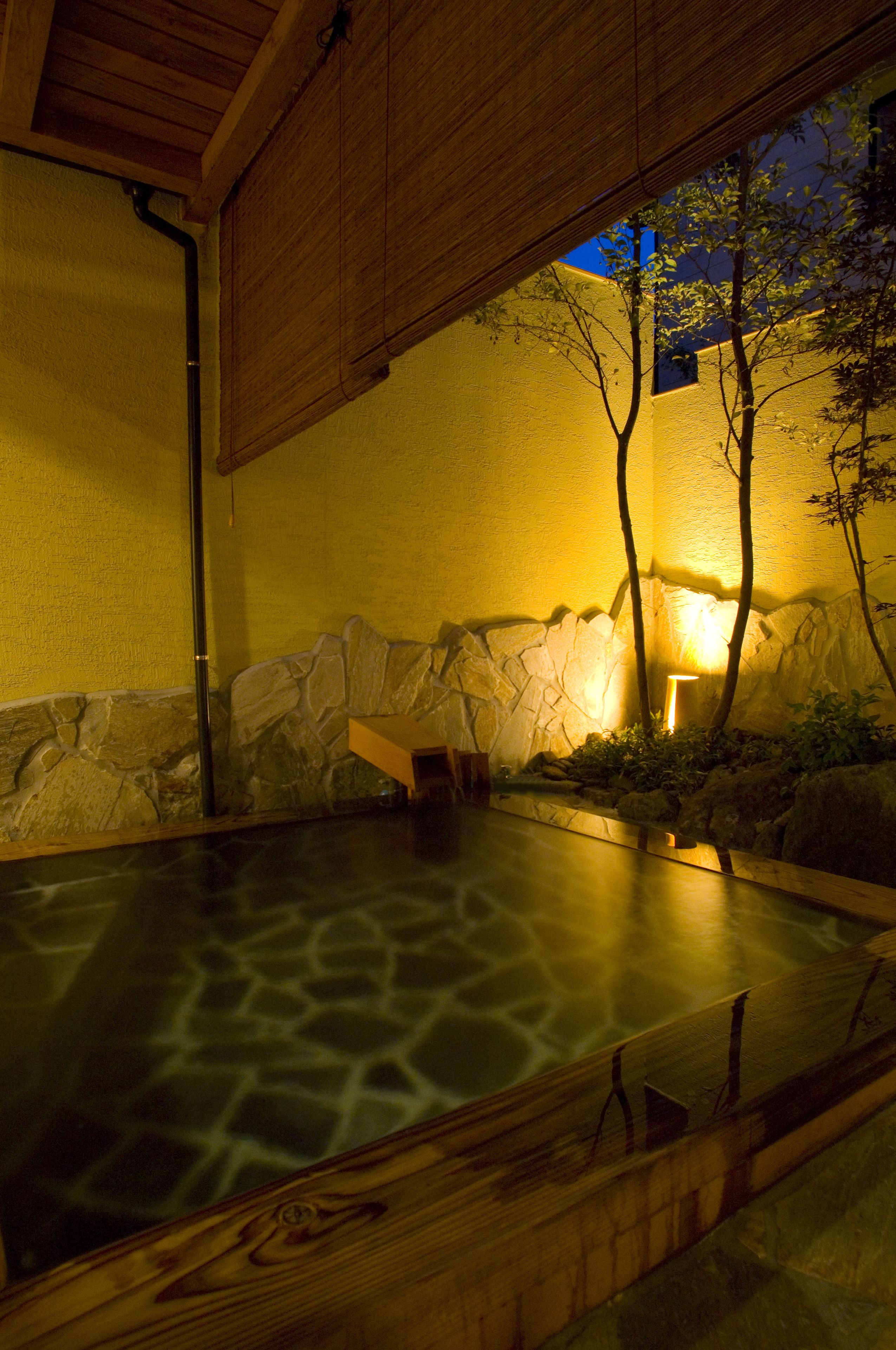 A hot spring area with a stone wall, wooden benches, and a lamp.