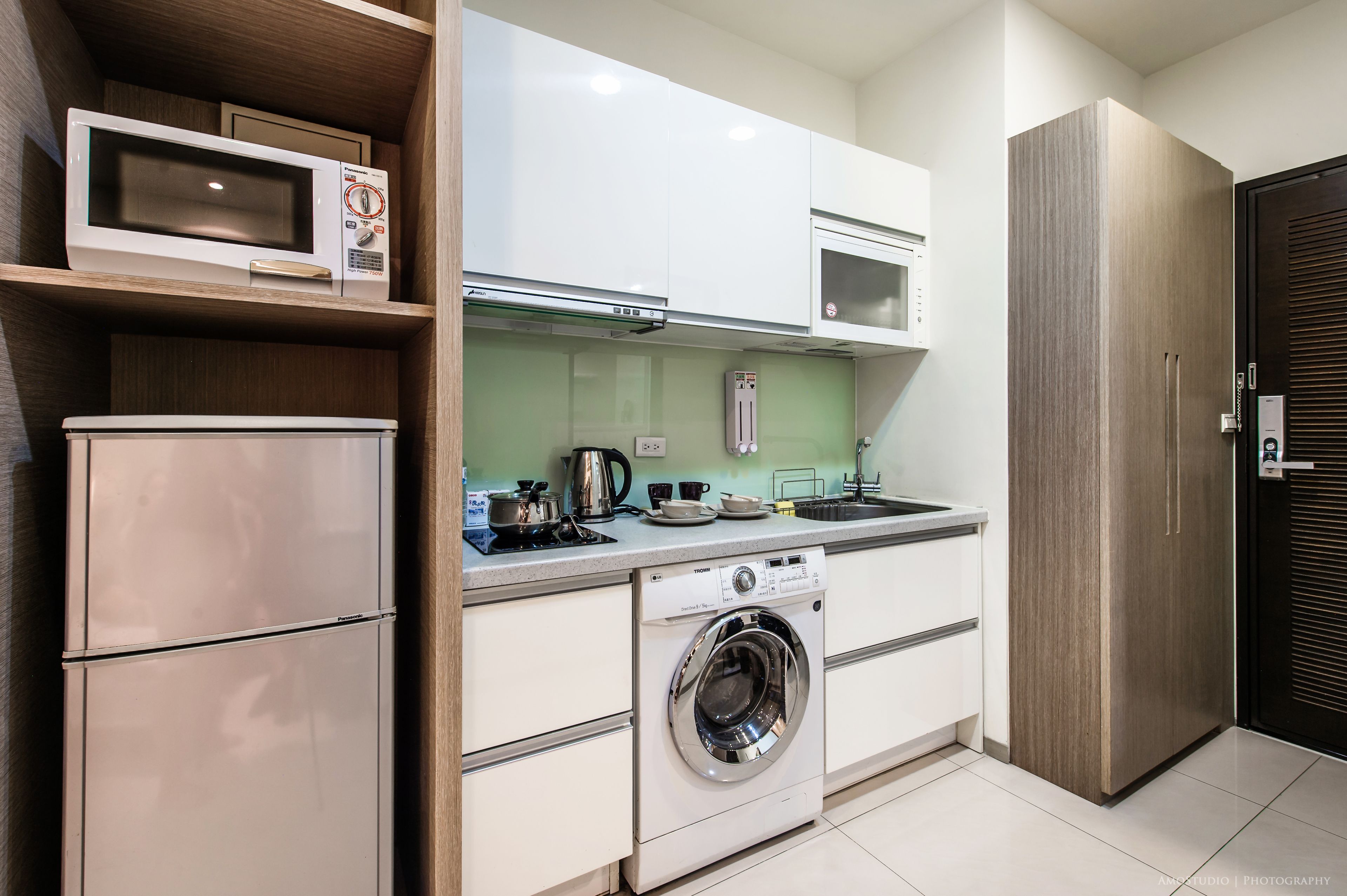 Une cuisine compacte équipée d’un four à micro-ondes, d’un four traditionnel et d’un lave-linge, avec des meubles de rangement en bois et un évier.