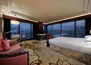 A hotel room with a large bed, a seating area with a sofa and armchairs, a small table, and a TV. The room has large windows offering a city view. - Sanding New Century Grand Hotel Yiwu (Jinhua)