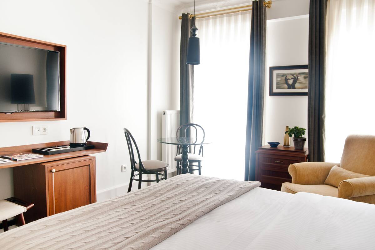 Una camera d'albergo con un letto, una scrivania con un computer, una sedia, un tavolo e una finestra con tende.