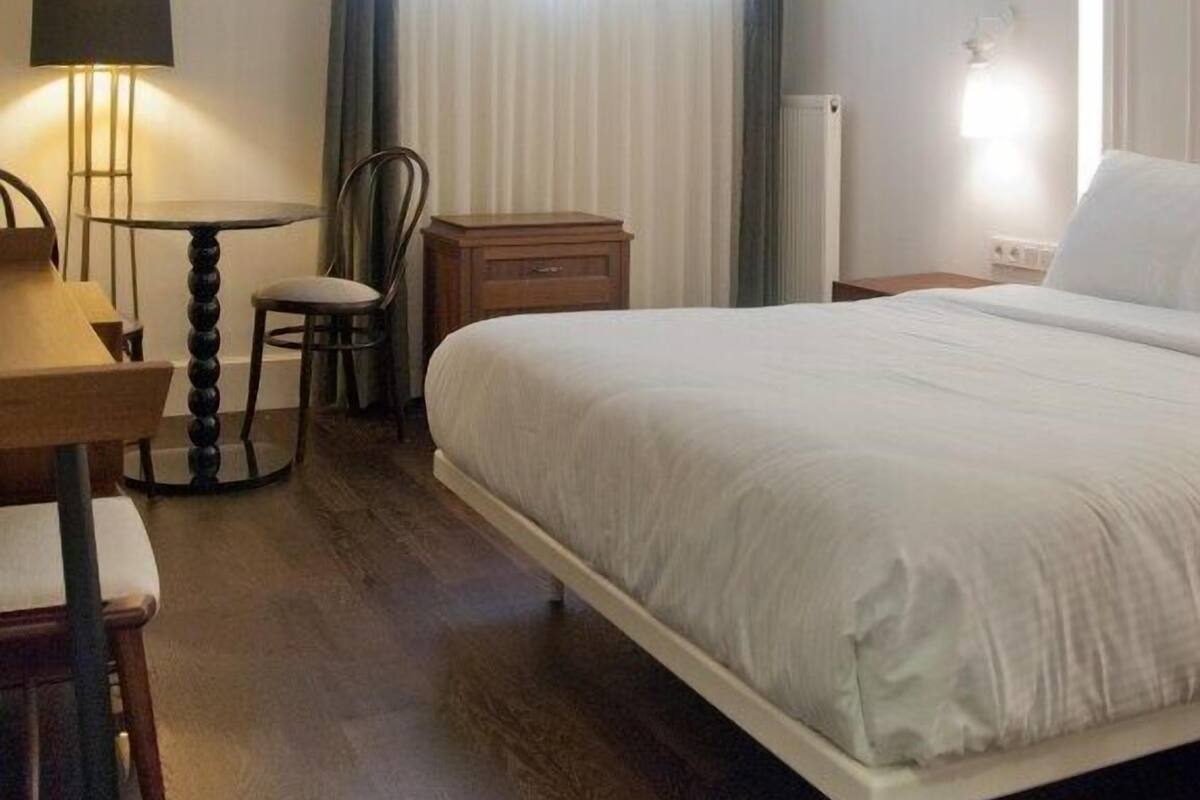 Una camera d'albergo con un letto, una scrivania con lampada, una sedia e una finestra con tende.