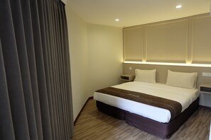 Quarto de hotel com uma cama grande, uma mesa de cabeceira e uma prateleira na parede.