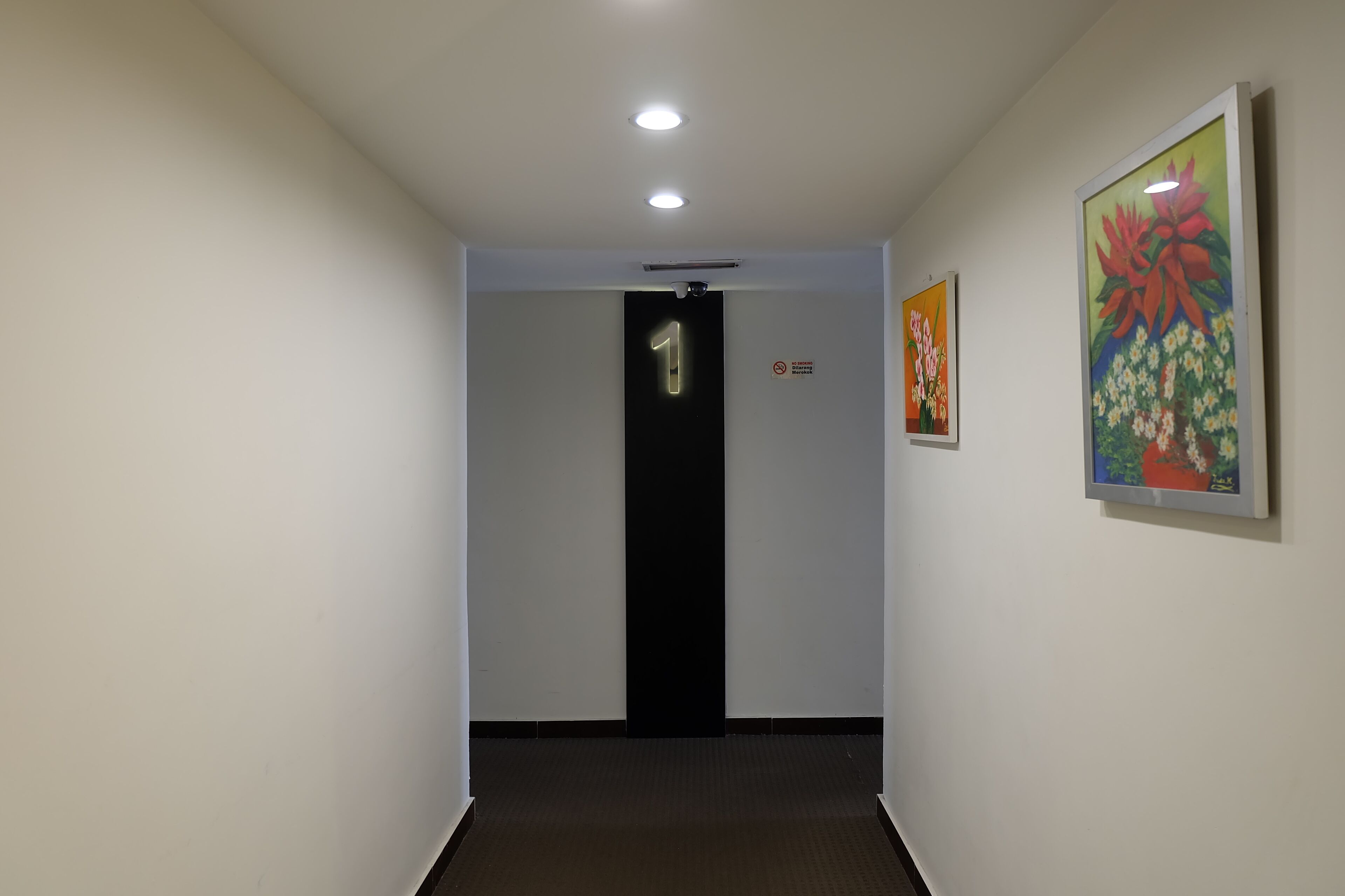 A hallway with a door marked '1', a no-smoking sign, and a framed floral painting on the wall.