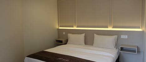 A hotel room with a large bed, bedside tables, and a wall-mounted shelf.