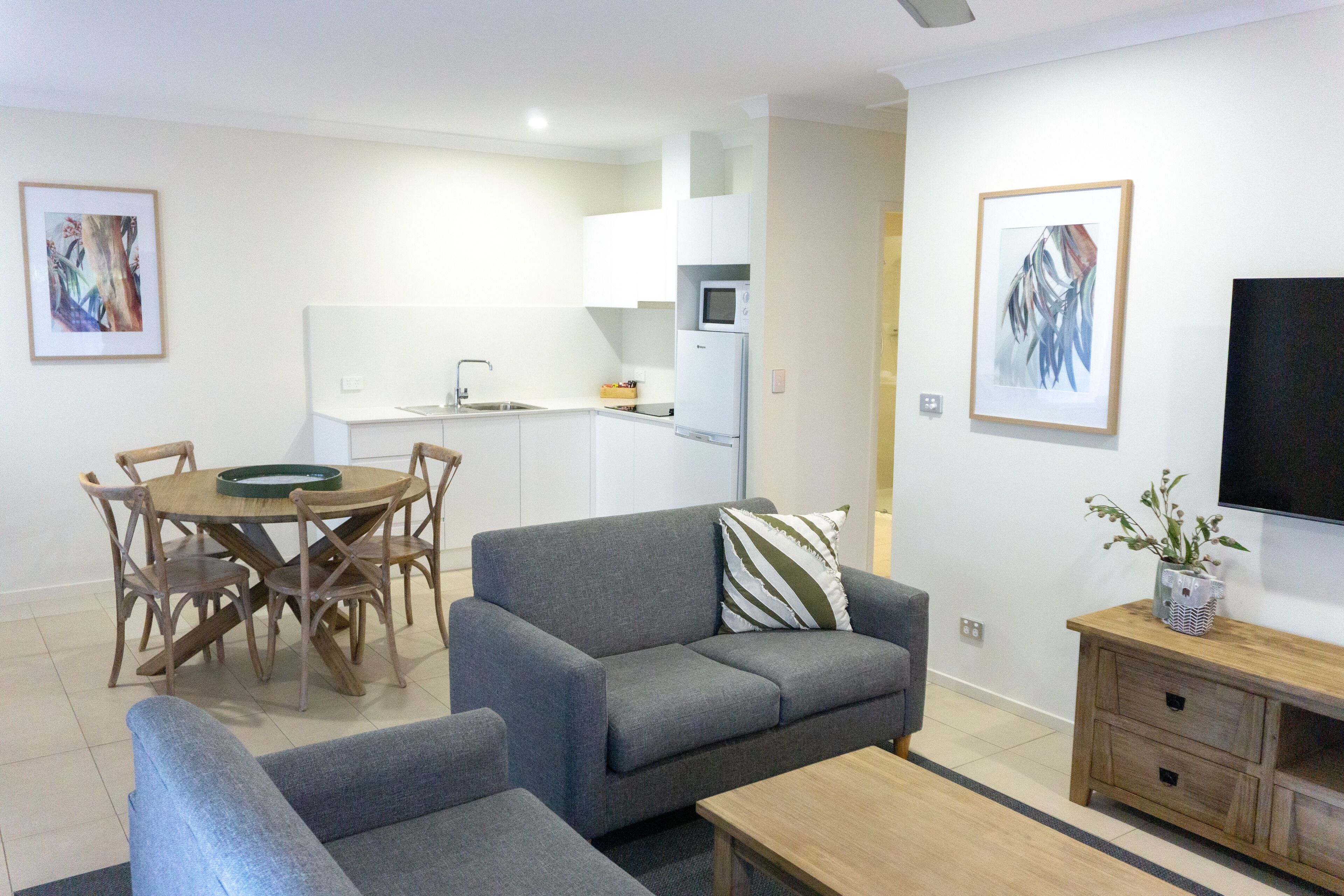 A modern living room with a grey sofa, a wooden coffee table, and a dining area with a wooden table and chairs.