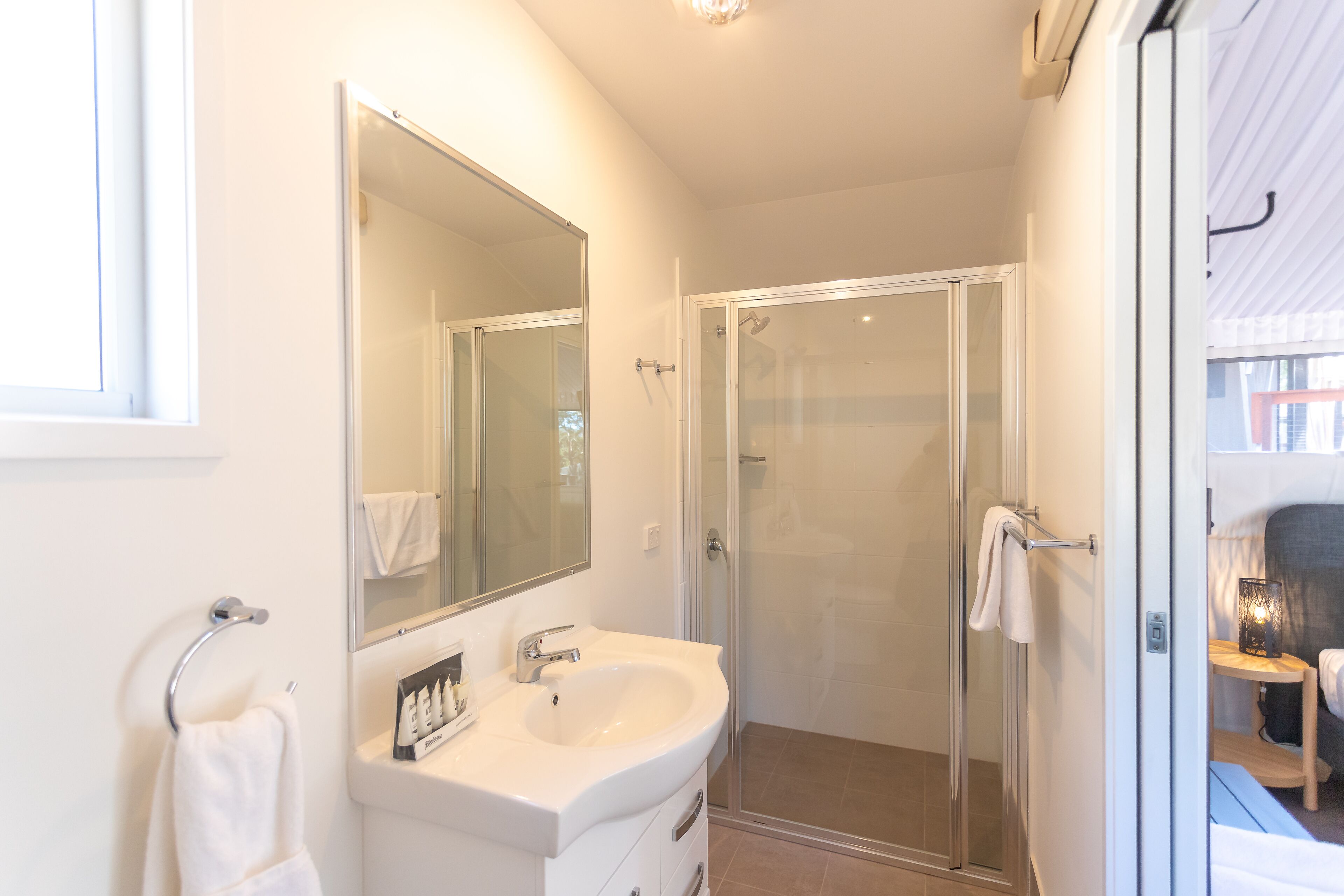 Une salle de bain avec un lavabo blanc, un miroir et une cabine de douche en verre.