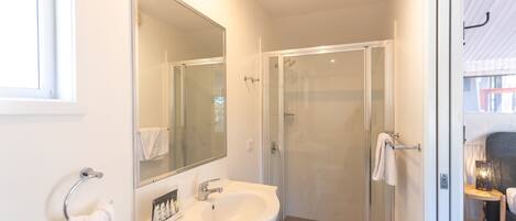 Une salle de bain avec un lavabo blanc, un miroir et une cabine de douche en verre.
