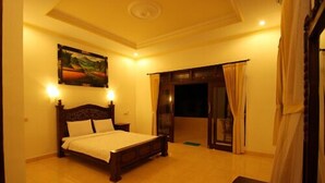 A bedroom with a bed, a painting, a nightstand, and a view through a door. - Tanah Semujan Ubud (Ubud)