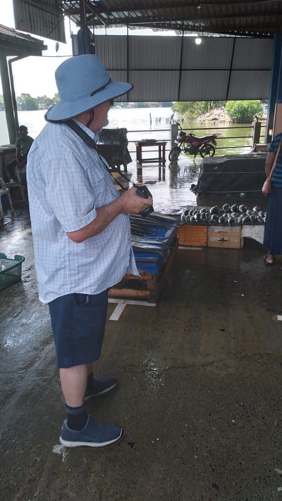 A person standing in a covered area with a table displaying various items, possibly for sale.