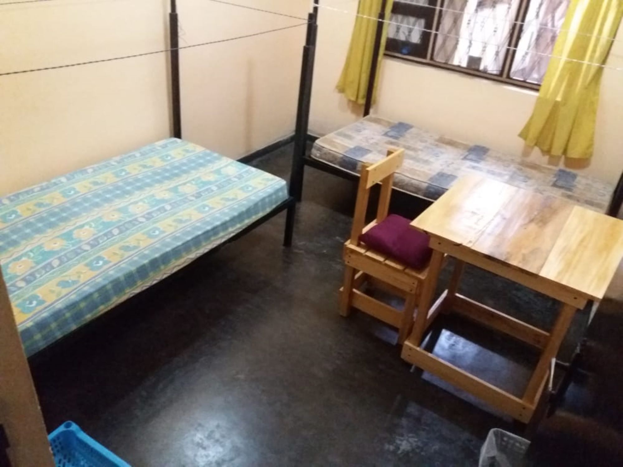 A small, compact room with a single bed, a wooden chair with a cushion, and a small table.