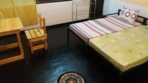 Een kleine kamer met een bed, een houten tafeltje, een stoel en een raam met gordijn.