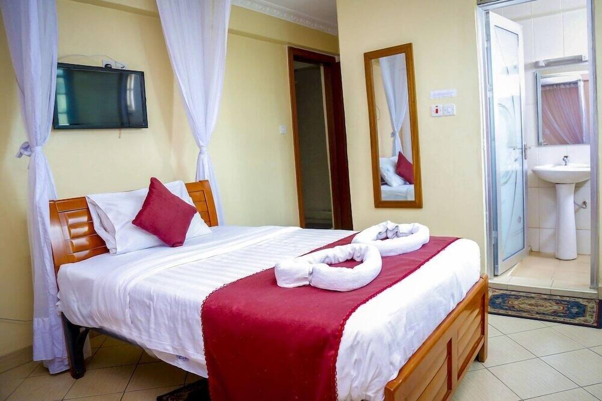 Habitación de hotel con cama, televisor, baño con lavamanos y espejo, y ducha.