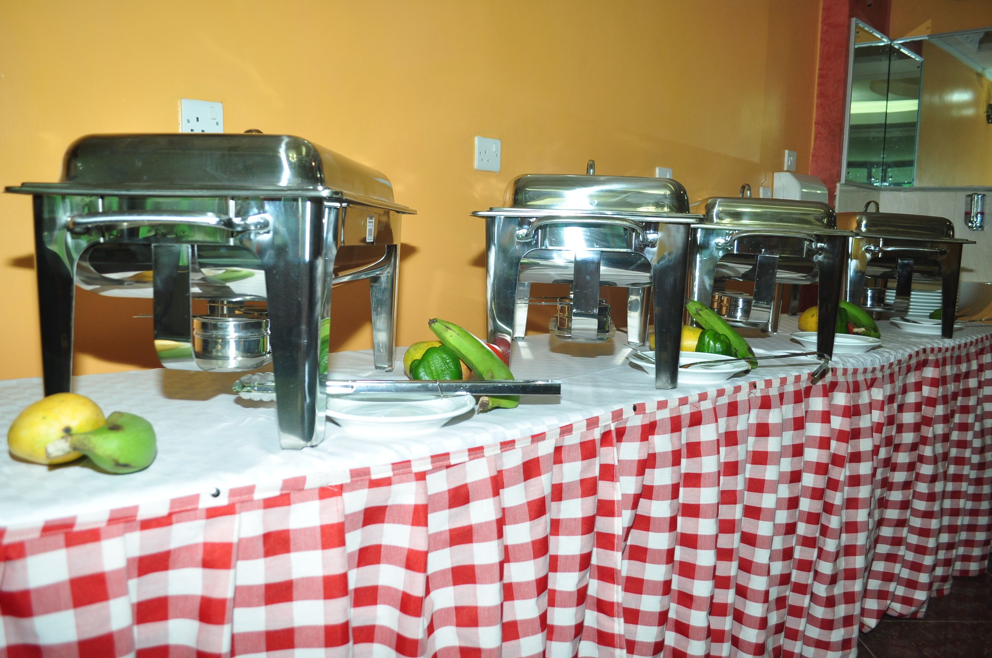 A buffet setup with multiple serving stations, a checkered tablecloth, and a yellow wall in the background.