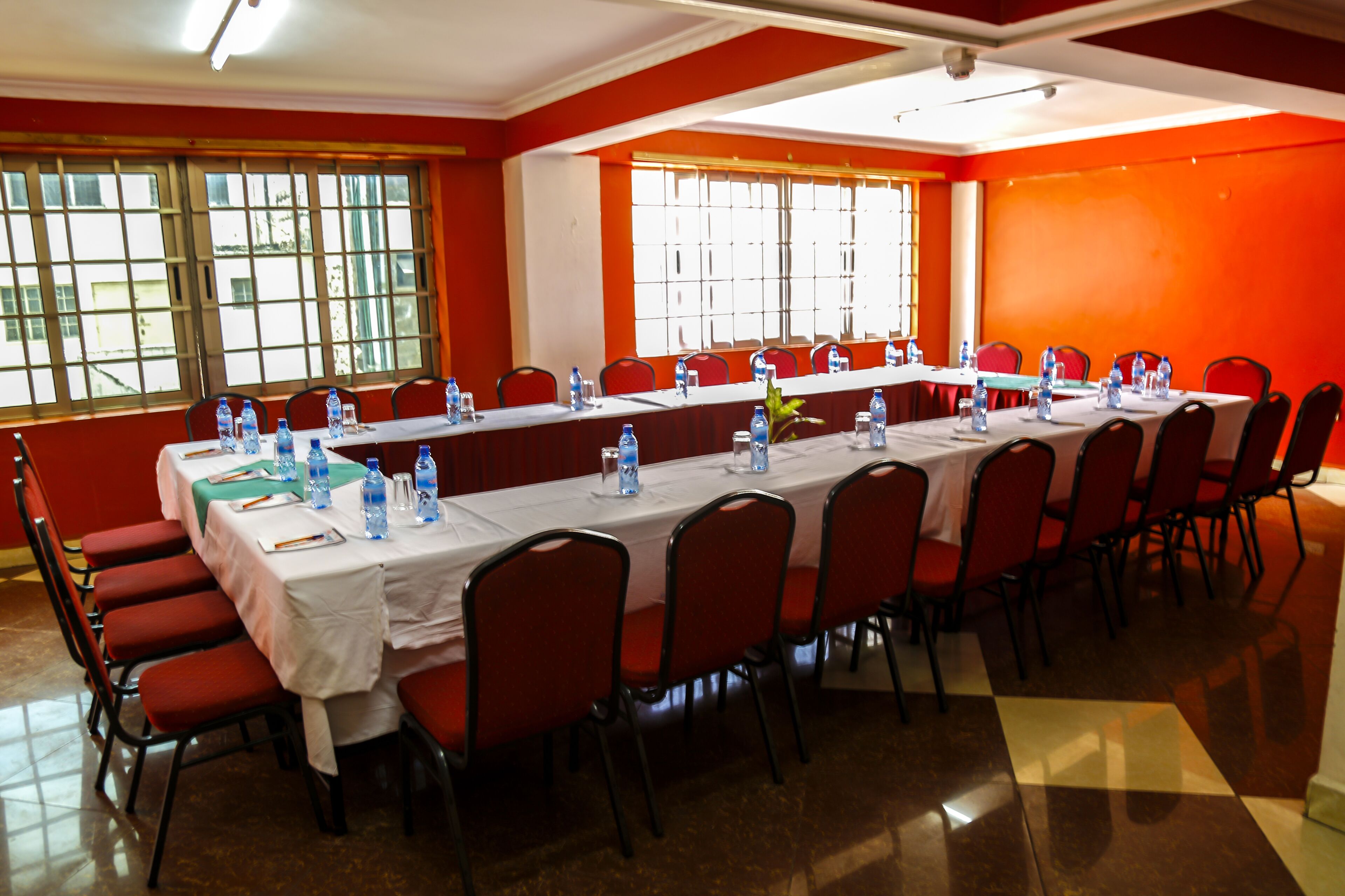 Une salle de conférence avec une longue table, des chaises rouges et des bouteilles d’eau posées sur la table.