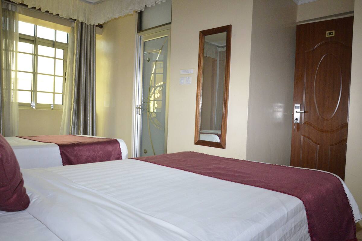 Habitación de hotel con dos camas, una puerta de madera y una ventana con cortinas.