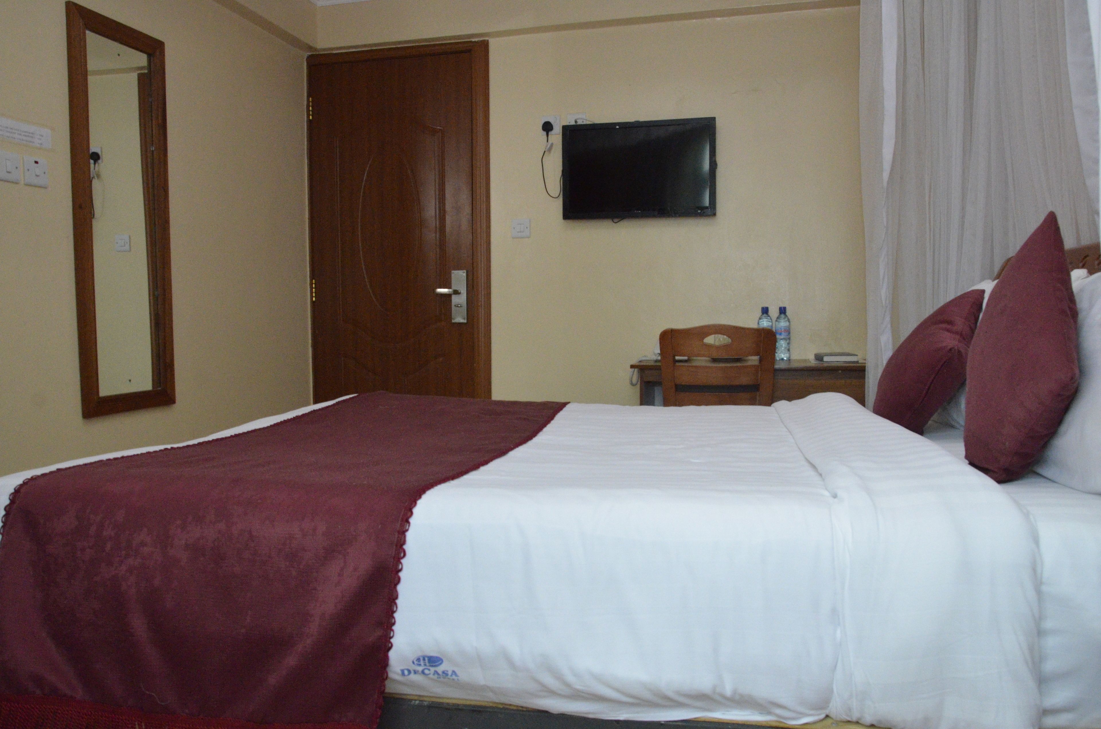 Een hotelkamer met een bed, een televisie, een bureau met een stoel en een spiegel.