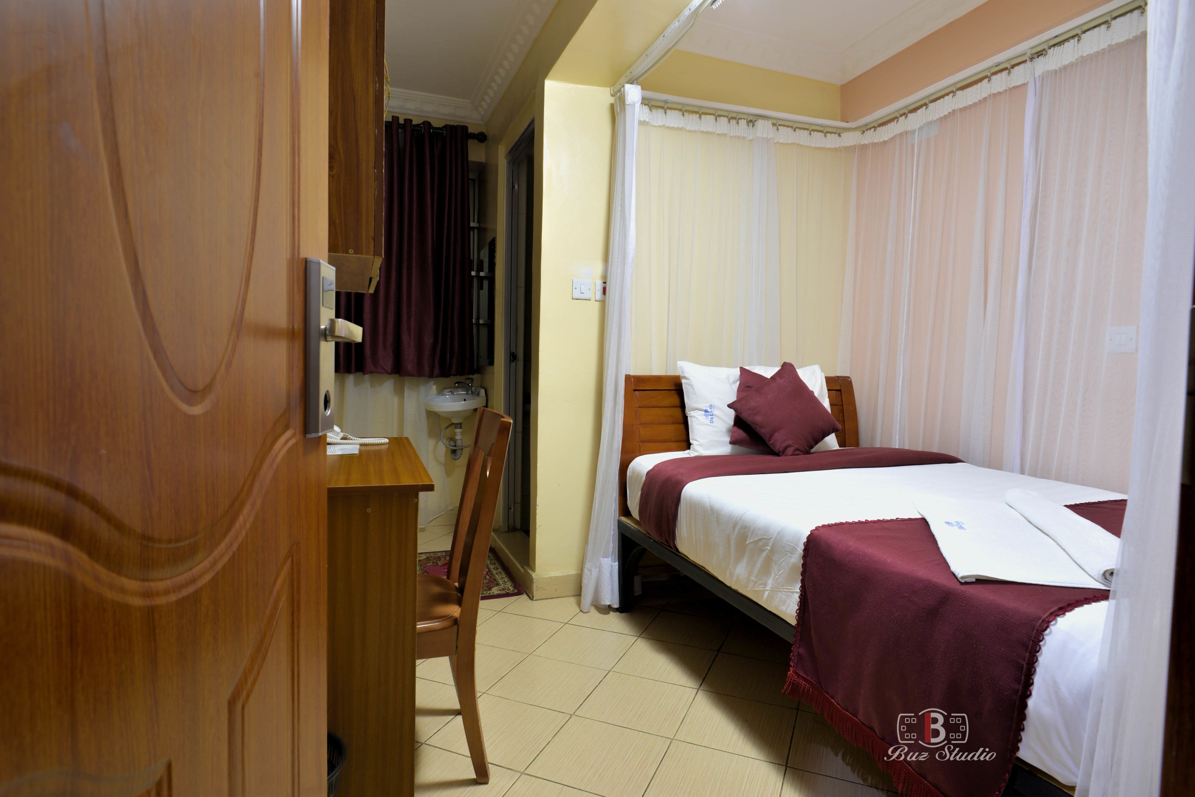 A hotel room with a bed, a chair, a desk, and a window with curtains.
