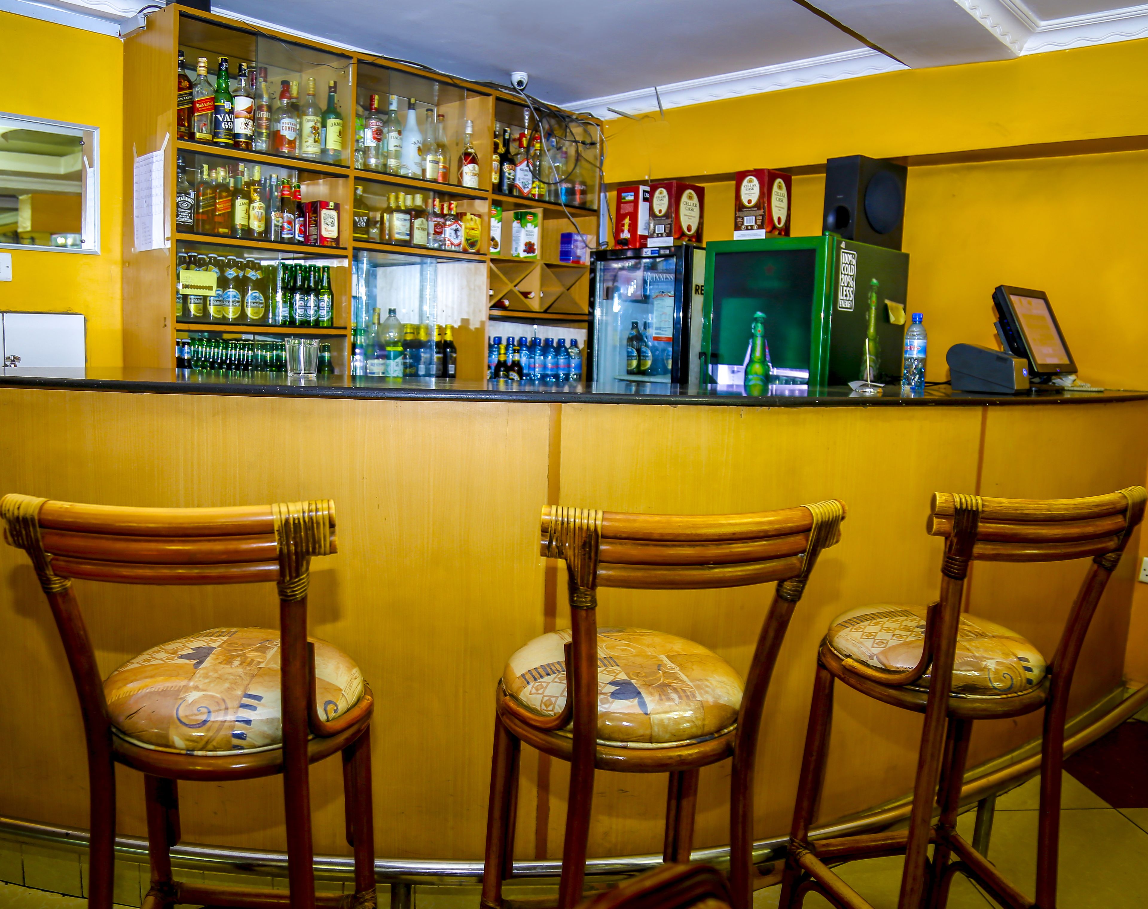 Una zona de bar con sillas de madera, una barra con varias botellas y un refrigerador verde.
