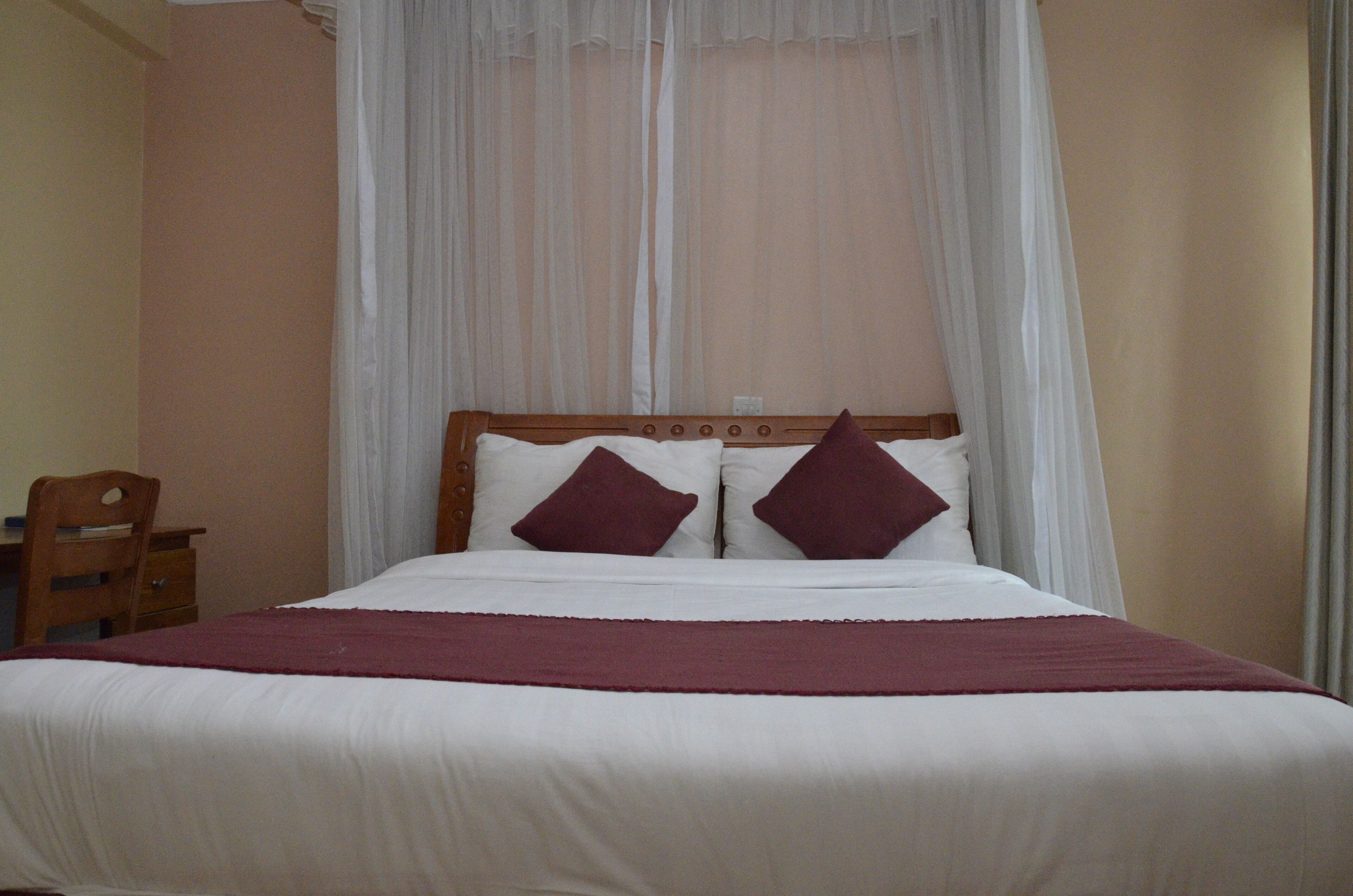 A bed with white bedding and two dark pillows, a wooden headboard, and a white canopy.