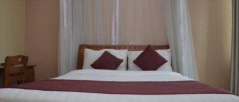 Una cama con ropa blanca, dos almohadas oscuras, un cabecero de madera y un dosel blanco.
