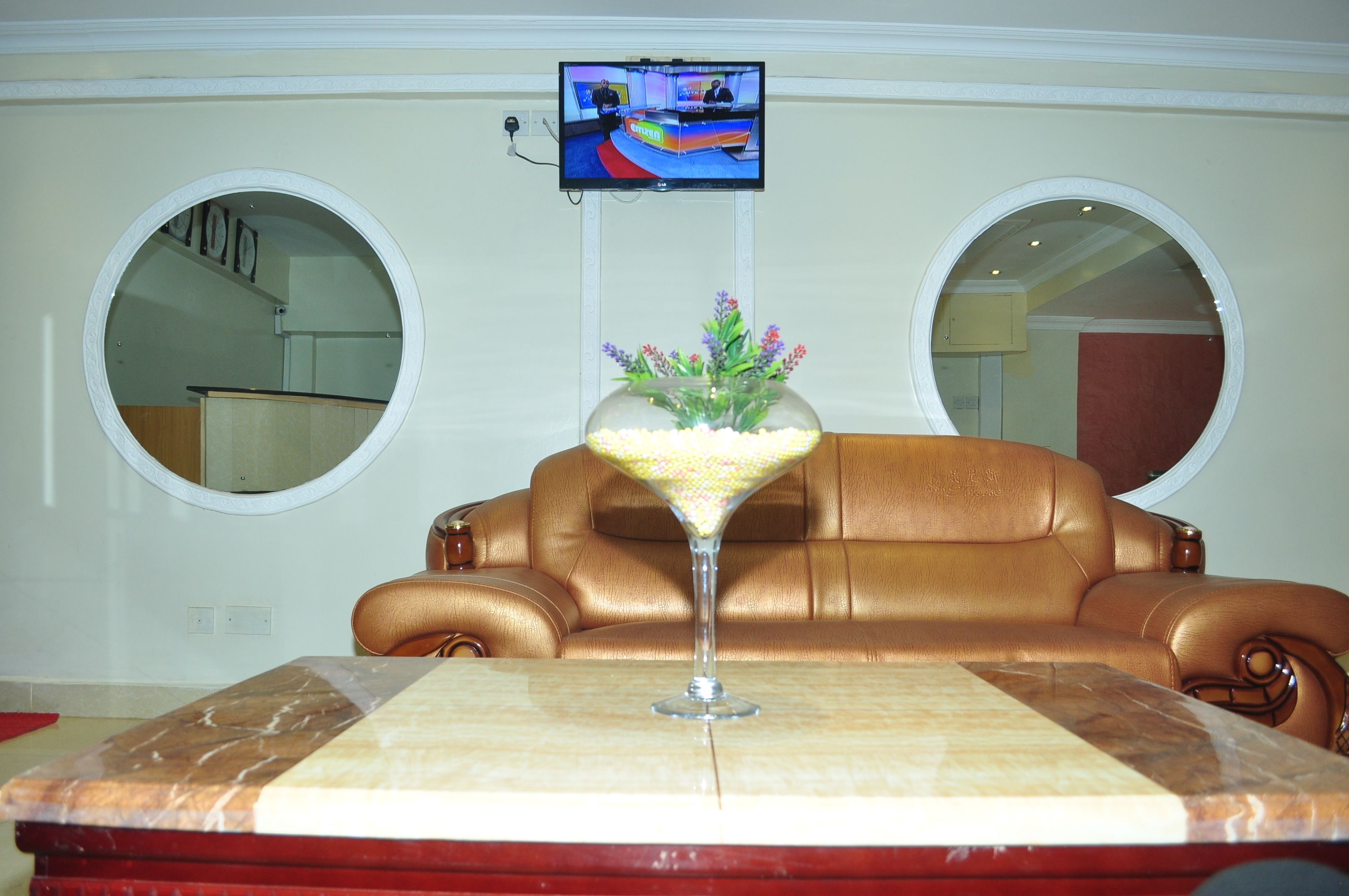 Una habitación con un sofá de cuero marrón, una mesa con cubierta de mármol y un televisor montado en la pared.