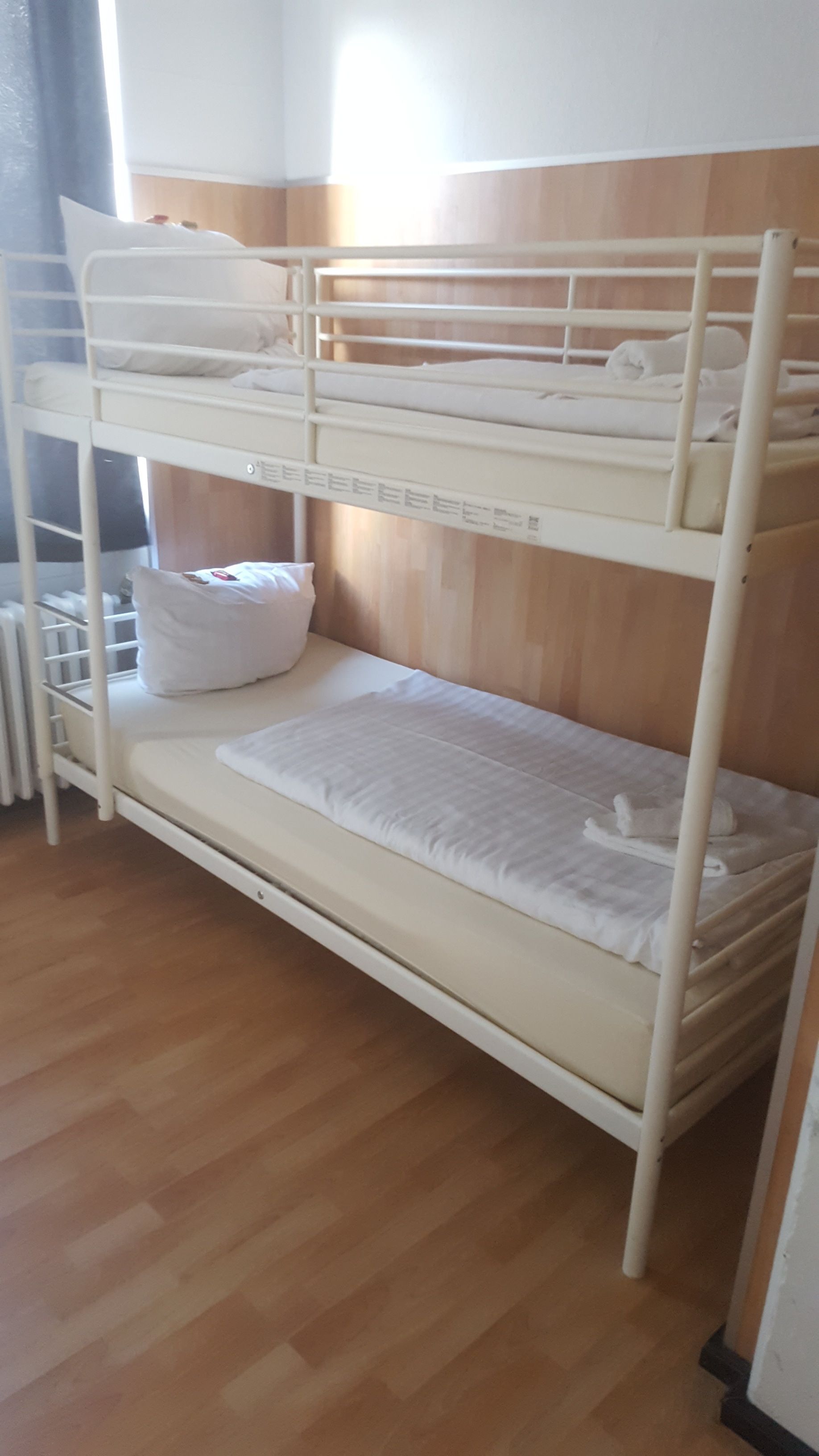 A bunk bed with white bedding, a wooden headboard, and a radiator below.