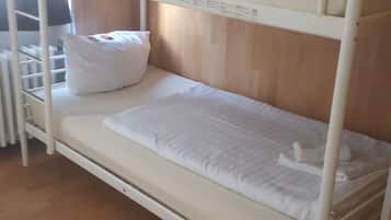 Un lit superposé avec une literie blanche, une tête de lit en bois et un radiateur en dessous.