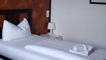 Een hotelkamer met twee bedden, een houten hoofdbord, een nachtkastje, een lamp en een lijst met een foto aan de muur.