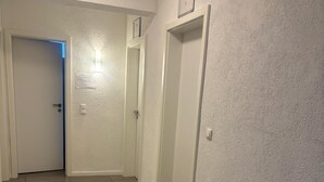 Un couloir doté d’un sol carrelé, de murs blancs et de portes donnant sur différentes pièces.