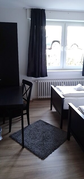 Una habitación con cama, escritorio, silla, radiador y ventana con cortinas.