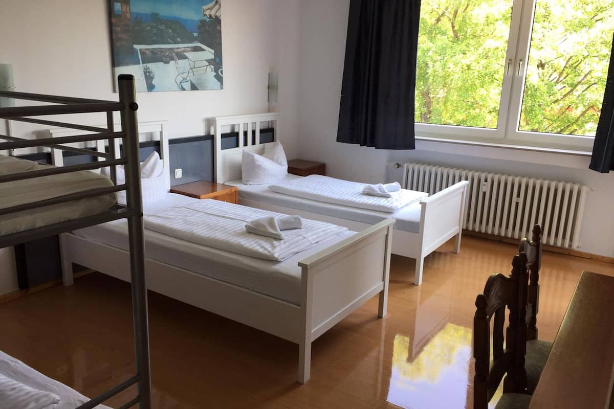 Habitación de hotel con literas, una cama individual, un radiador, una ventana con cortinas y un cuadro en la pared.