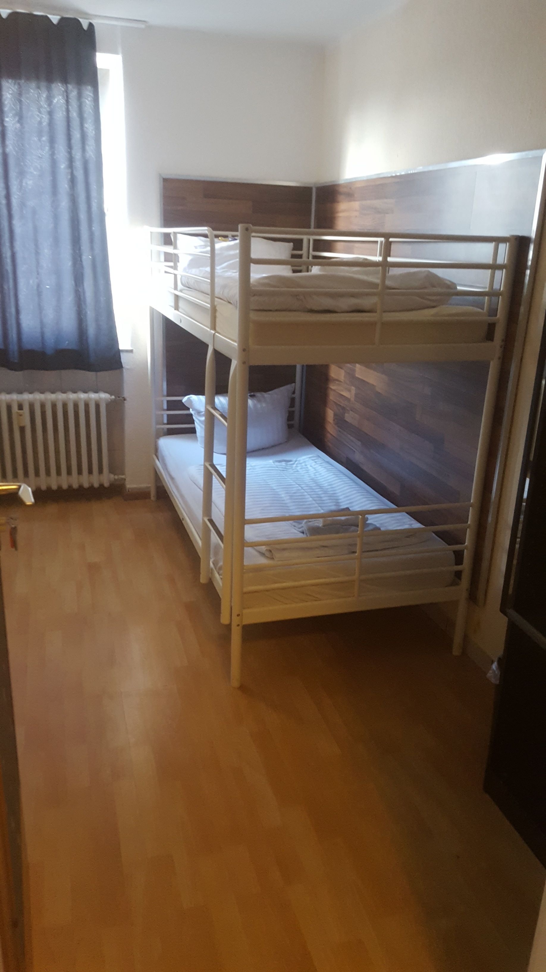 Habitación con literas, piso de madera, un radiador y una ventana con cortinas.