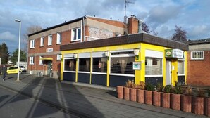 Une auberge de jeunesse à la façade jaune, dotée de grandes fenêtres, avec un bâtiment en briques en arrière-plan.